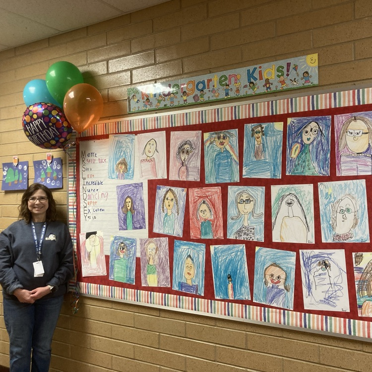 Mrs Lindsey standing by the bulletin board of all of the portraits students drew of her