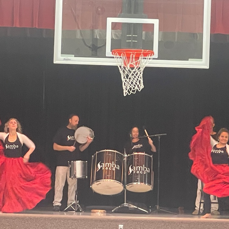 two men drumming in the middle and two women in flowing red skirts dancing on either side
