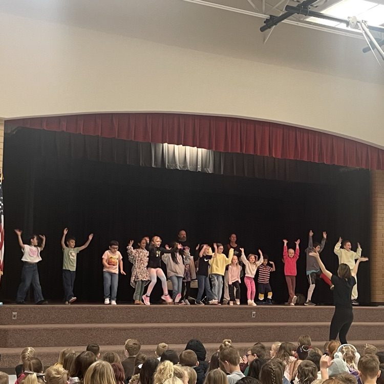 many students dancing on the stage being led by a woman in the front