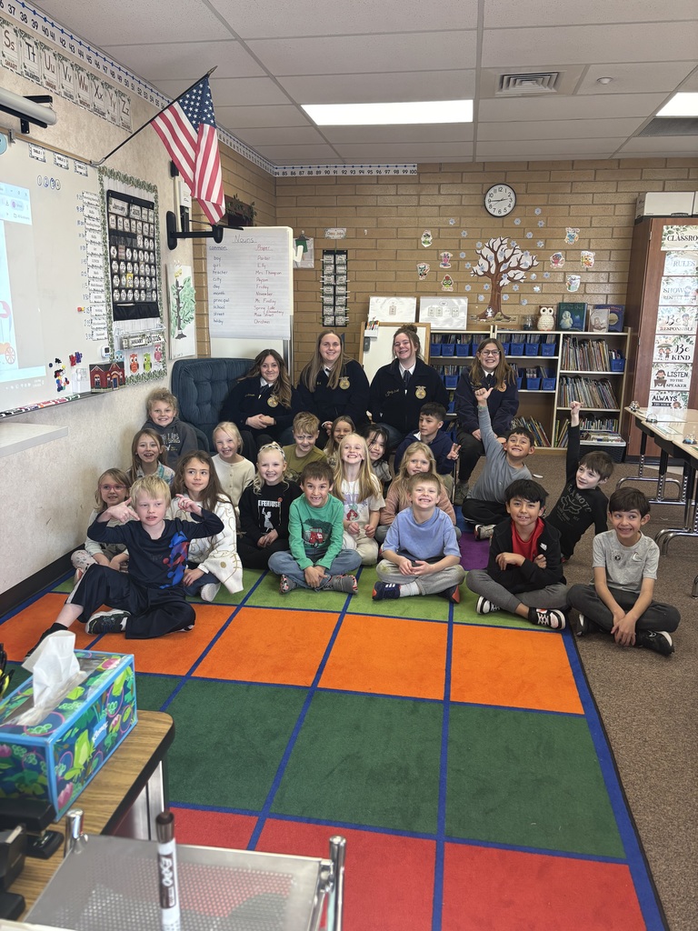 a second grade class sitting on the rug in front of 4 FFA students
