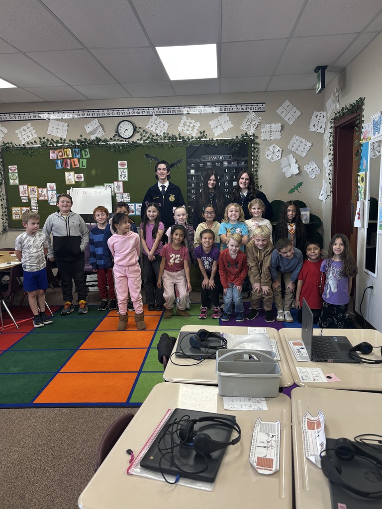 a second grade class standing in front of 3 high school FFA students
