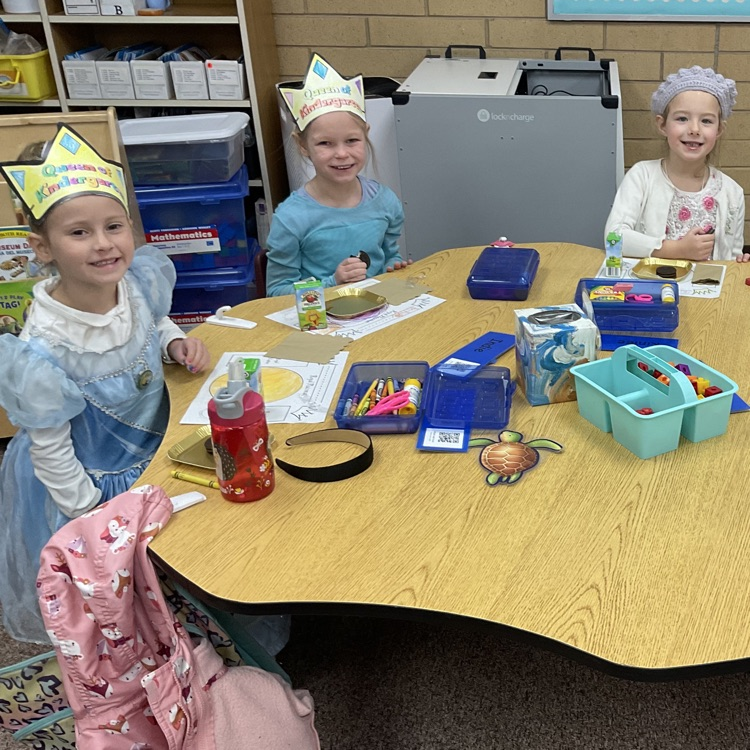 three girls sitting at a table with crowns on