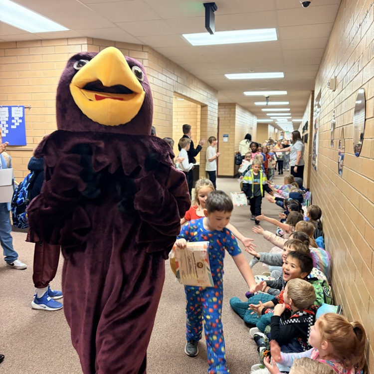a Hawk mascot being followed by a line of students who are giving high fives to other kids in the hall