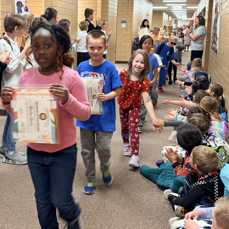 a line of kids walking down the hall while other kids cheer for them