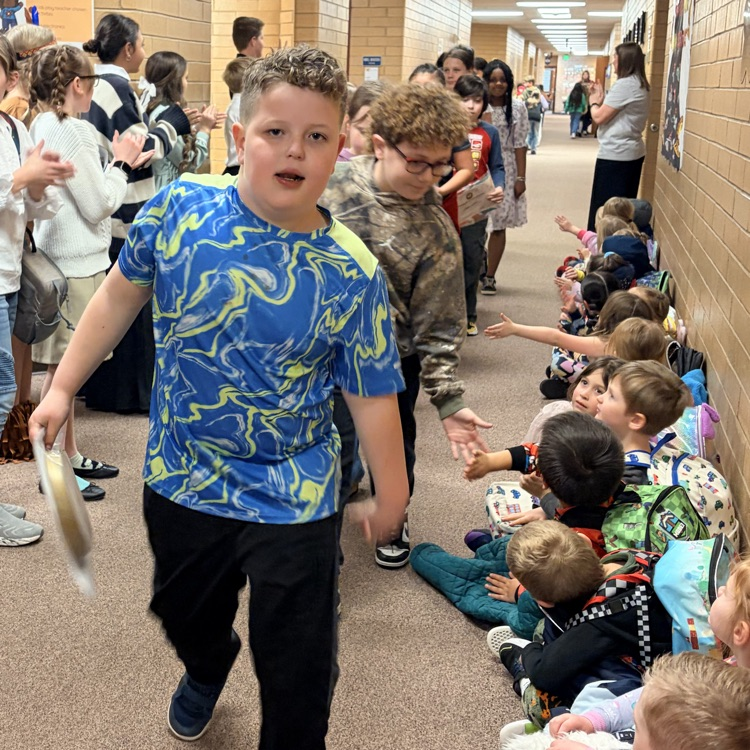 a line of kids walking down the hall while other kids cheer for them