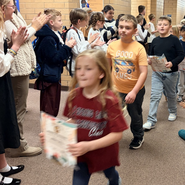 a line of kids walking down the hall while other kids cheer for them