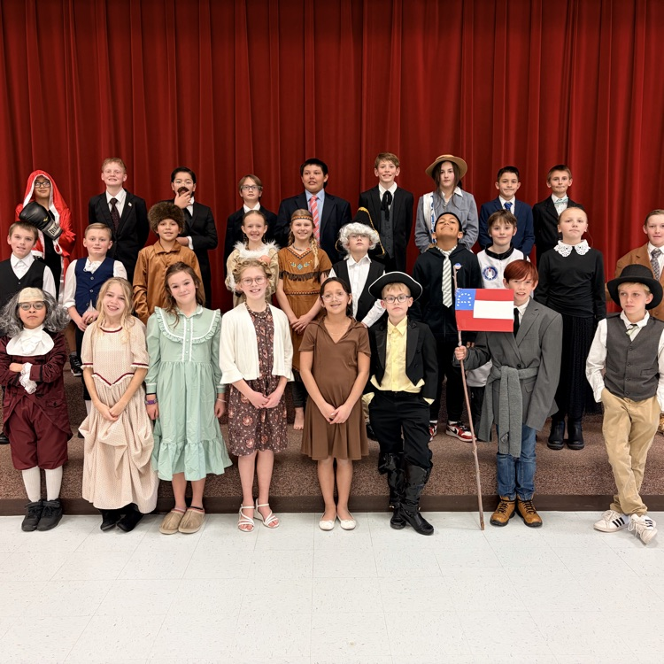 a fifth grade class lined on the gym steps and looking at the camera. each student was dressed as a famous American 