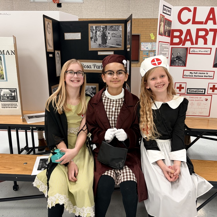 three students sitting in front of poster boards and dressed as to represent individuals from history