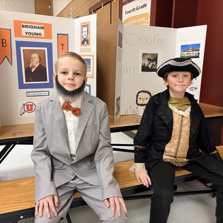 two students sitting in front of poster boards and dressed as to represent individuals from history