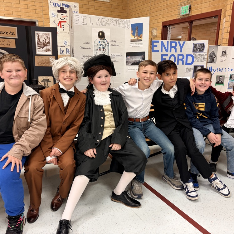 six boys sitting in front of poster boards and dressed as to represent individuals from history