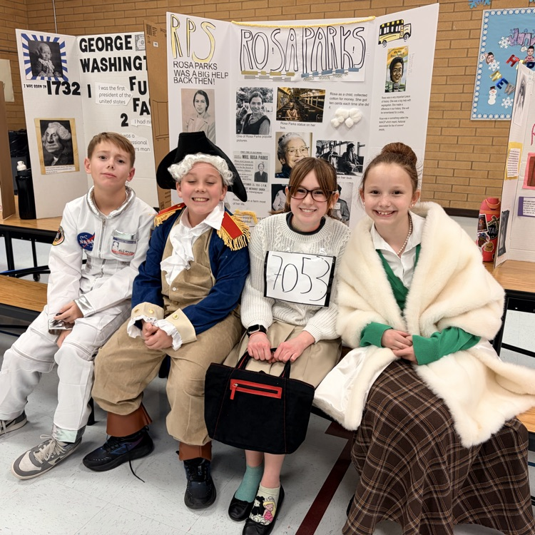 four students sitting in front of poster boards and dressed as to represent individuals from history