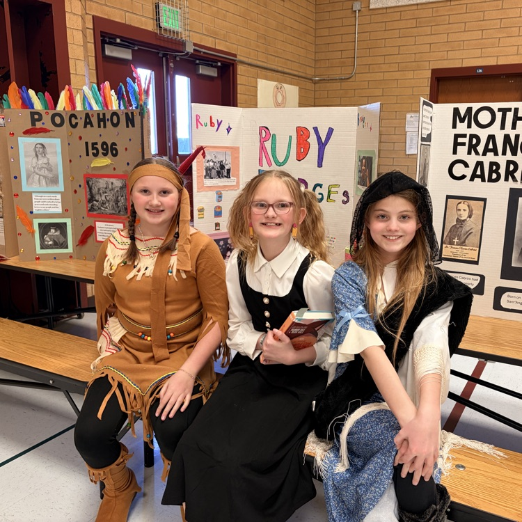 three girls sitting in front of poster boards and dressed as to represent individuals from history