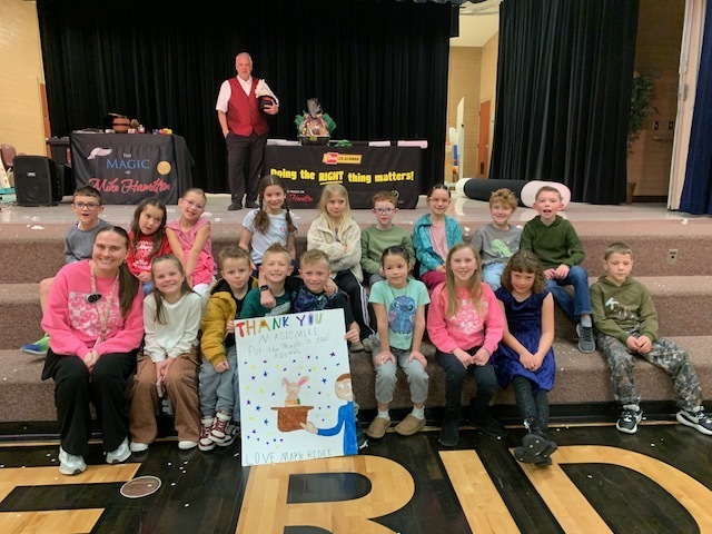 Magician, Mike Hamilton, posing with a class of 2nd graders and their thank you note.
