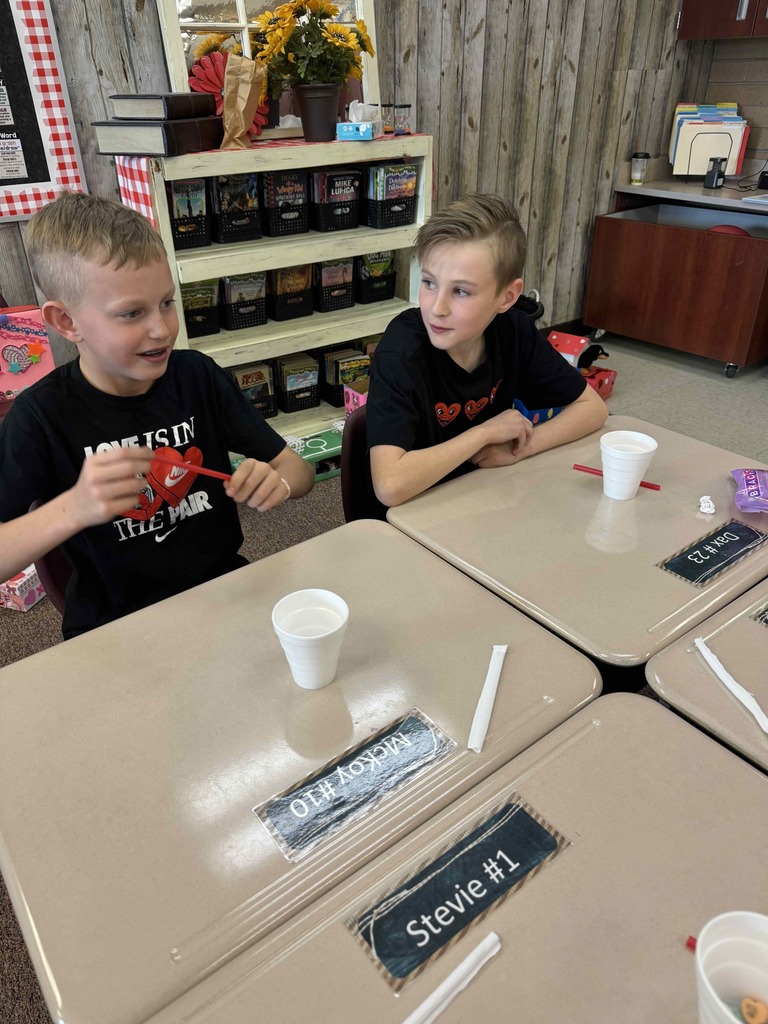 Two boys sitting at desks with cups and straws.