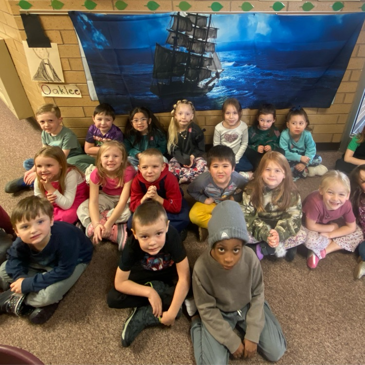 a group of kindergarten students sitting in front an image of a ship in the ocean