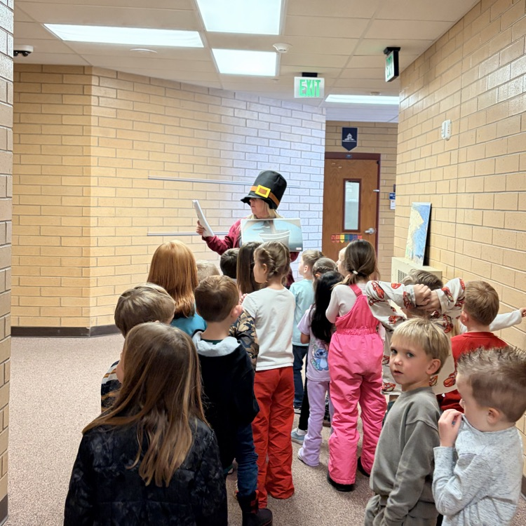 a teacher wearing a pilgrim hat and reading to kids who are standing in line 