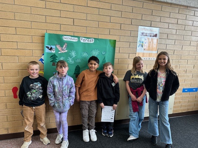 six students standing in front of a green poster entitled "deciduous forest" 