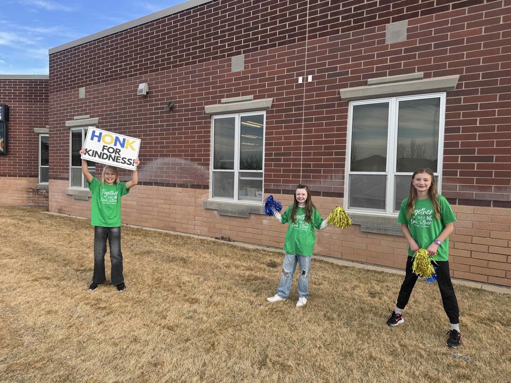 Students welcoming other students to school. One is holding a sign that says: Honk for Kindness.