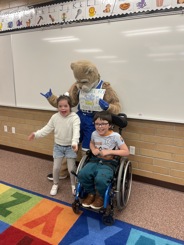 Cosmo posing with a couple of students holding a sign that says: I will be safe and kind online.