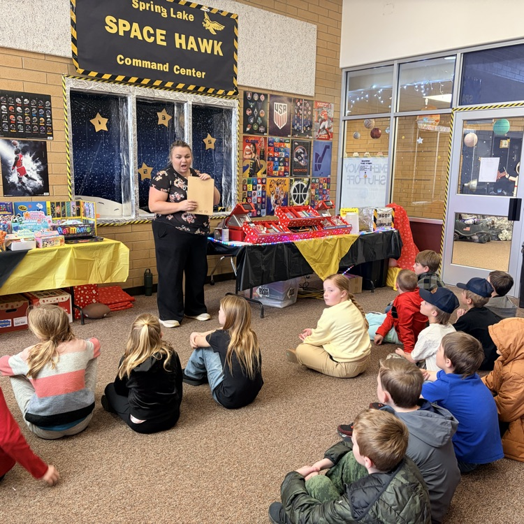 a member of the PTA explaining the book fair to a third grade class sitting on the floor