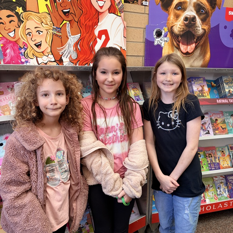 three girls smiling in front of book shelves