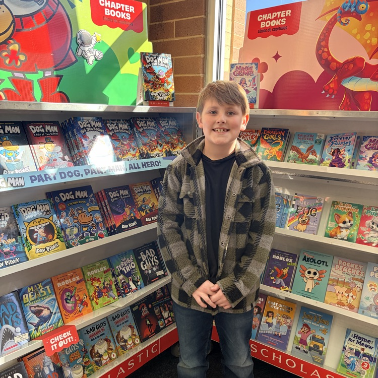 a boy smiling and standing in front of two bookshelves 