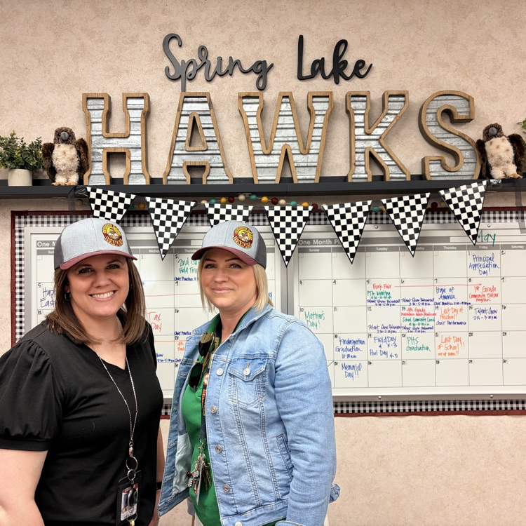 two secretaries standing in front of a whiteboard calendar and sign that says “spring lake hawks" 