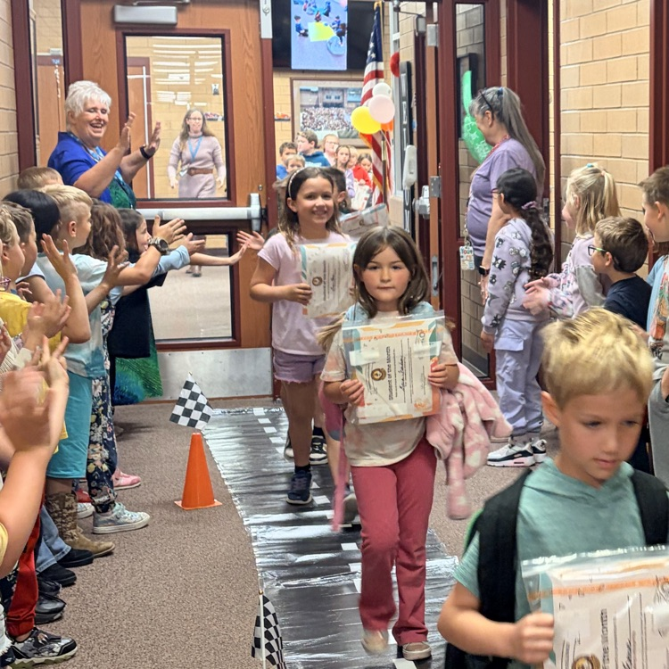 first grade students cheering on their classmates walking through the hall 