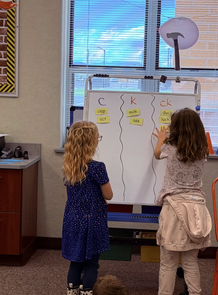 students working at the whiteboard together working on letters and words 