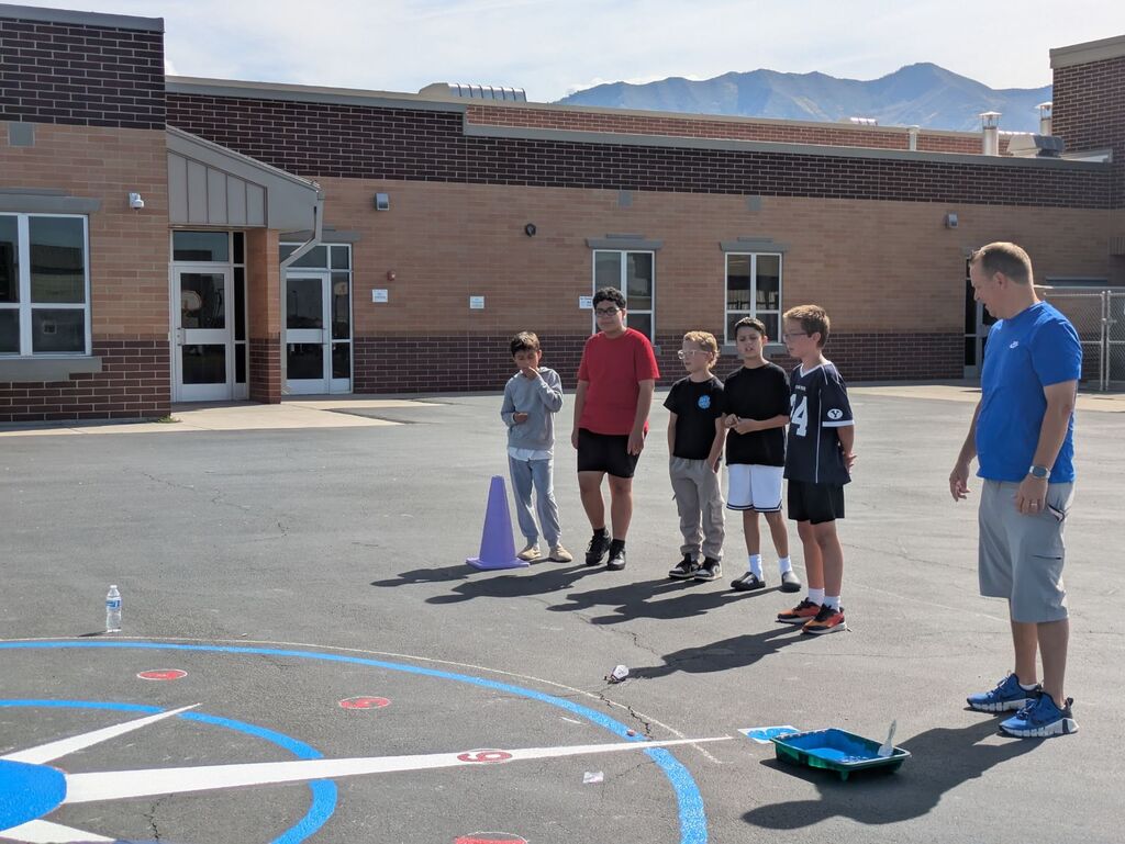 students watching an adult paint the blacktop