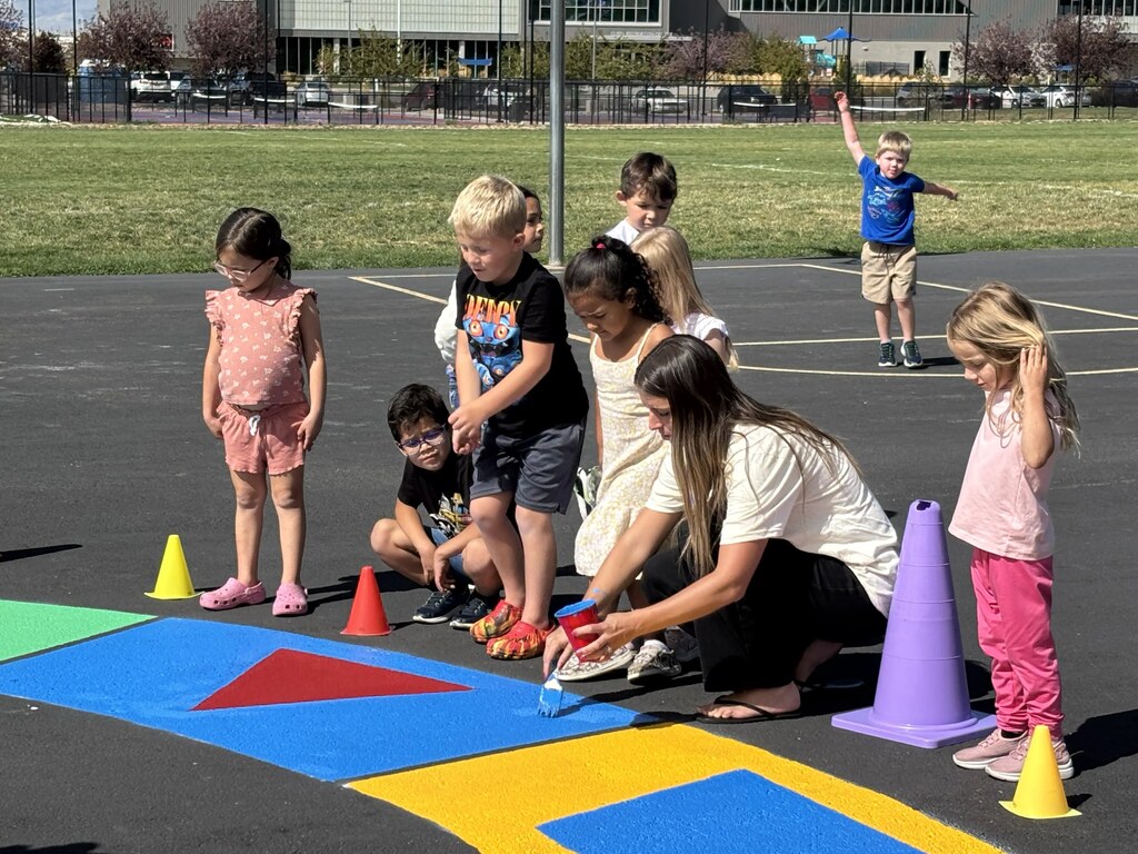 students watching an adult paint the blacktop
