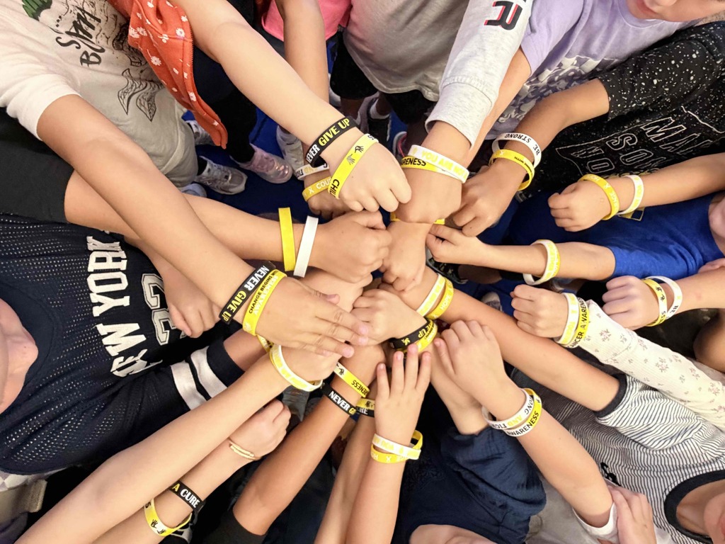 Students hands in a circle wearing yellow and white bracelets.