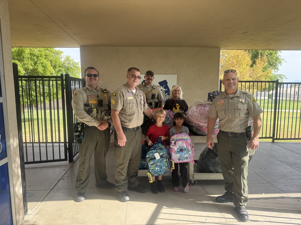Sherrifs posing with students and principal distributig back packs.