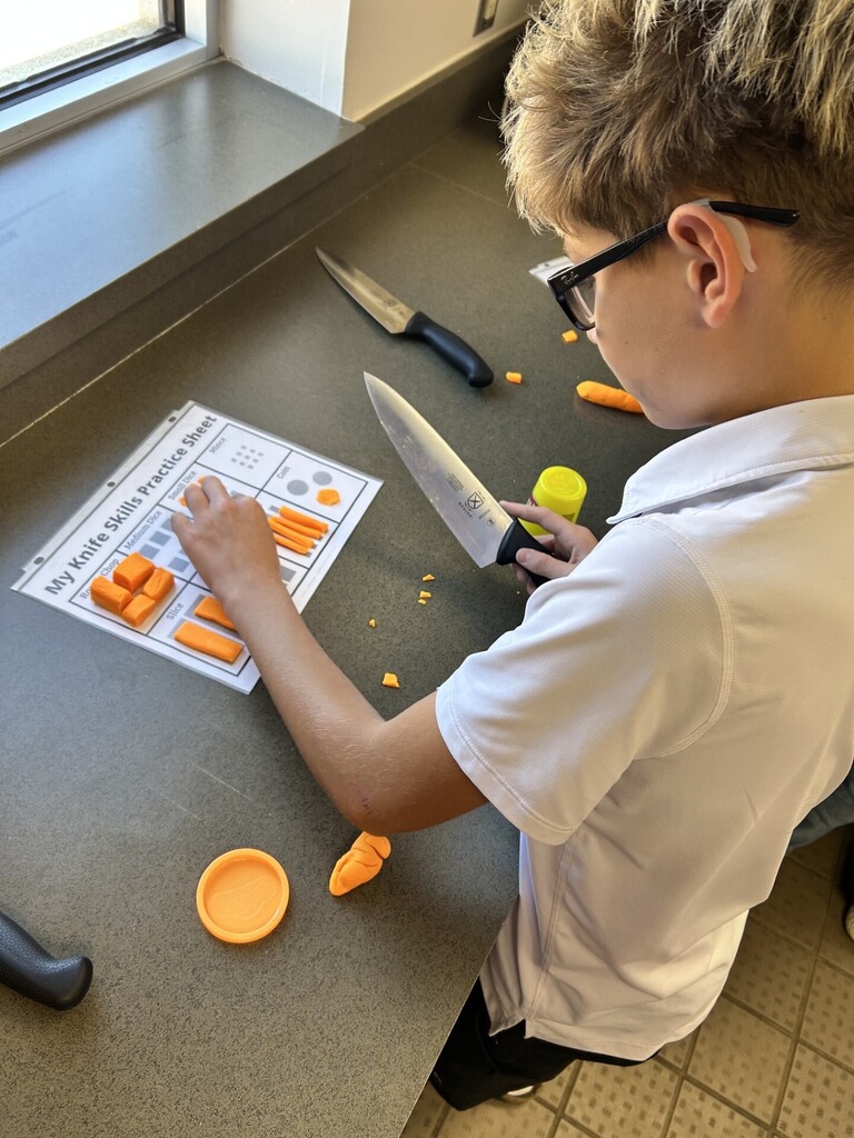 student in black glasses and blond hair cutting orange play-doh
