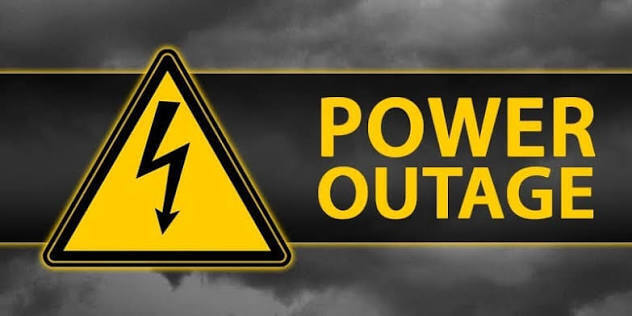 Yellow electrical hazard warning sign with a black lightning bolt beside bold yellow text reading “POWER OUTAGE” on a dark, stormy background.