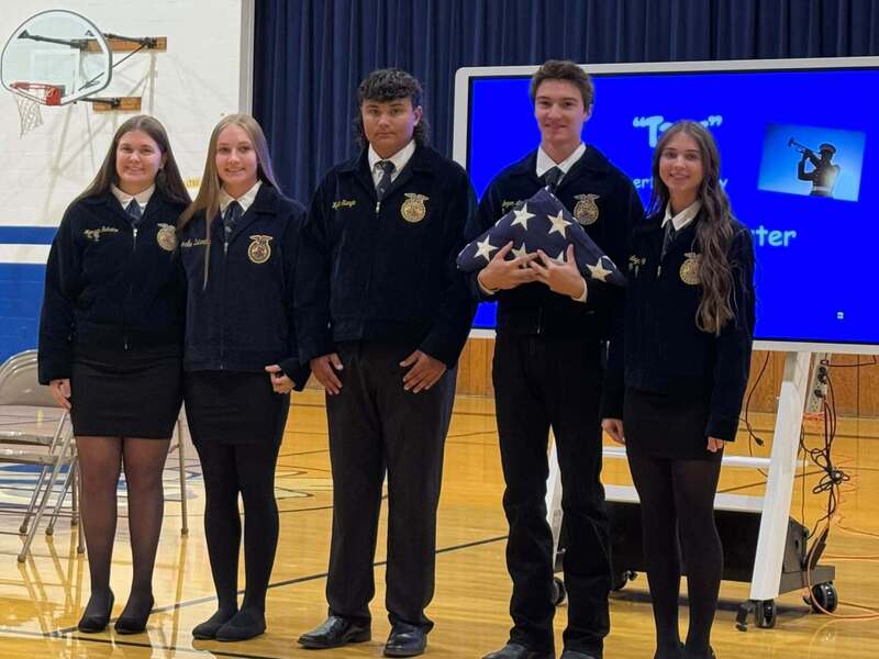 Five FFA students pose together in the school gym, with one student holding a folded American flag during the patriotic ceremony.