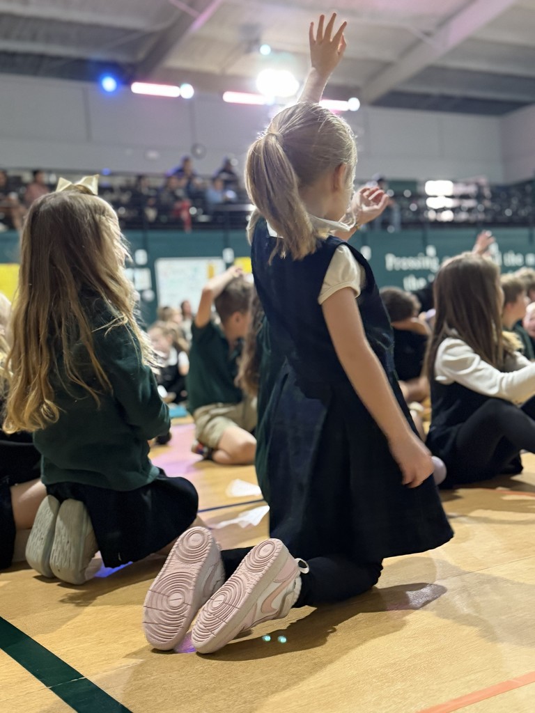girl sitting on her knees on the gym floor with her left and raised.