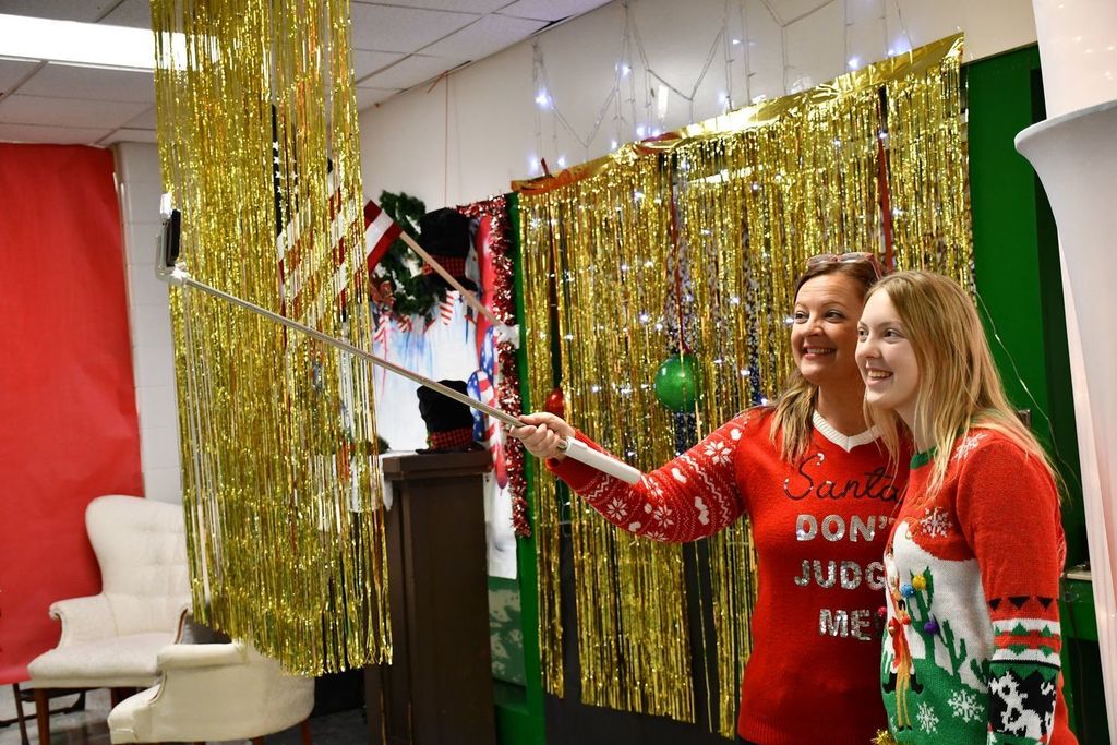 a parent and student taking a photo with a selfie stick in fun holiday sweaters