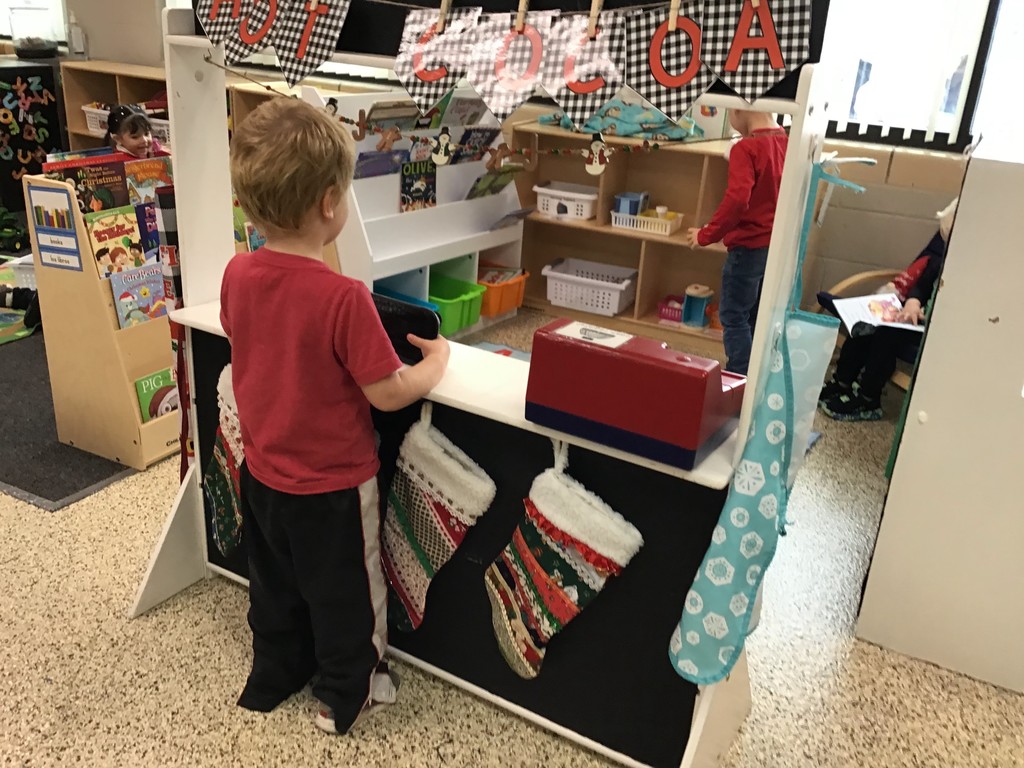 These three year olds have been busy in December! The students sorted in the sensory table with magnetic wands, jingle bells, tinsel, and pompoms. They played with their peers in the dramatic play center with a hot cocoa stand, Christmas baking, and a tree to decorate. In the writing center, the students wrote letters to Santa and  put them in the mailbox to send them to the North Pole. In art, the preschoolers painted with pine boughs and created their own reindeer directed drawing. So many engaging ways to learn and play with friends!