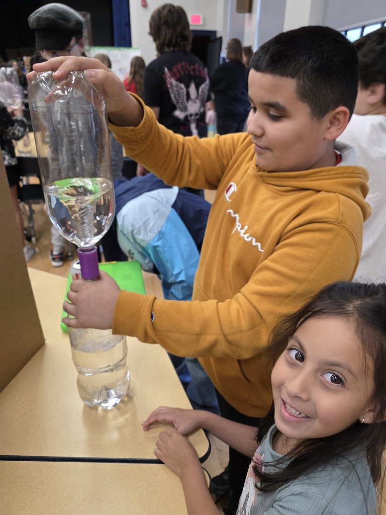 Two students at a table. One swirls a tornado in water inside a bottle.