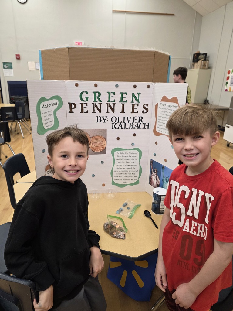 Two students stand in front of a green pennies science fair board.