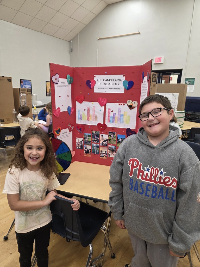Two students standing in front of a red science fair poster board.