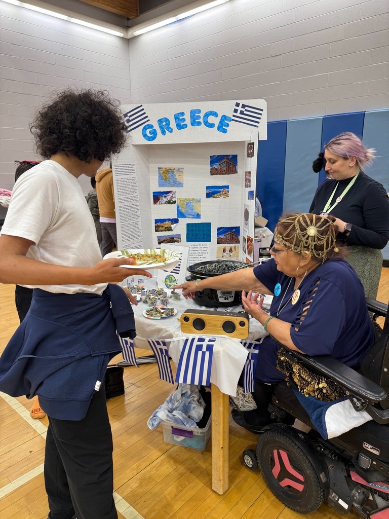 multi cultural night at the greece table we see a participant reading the display board while two women highlight the information