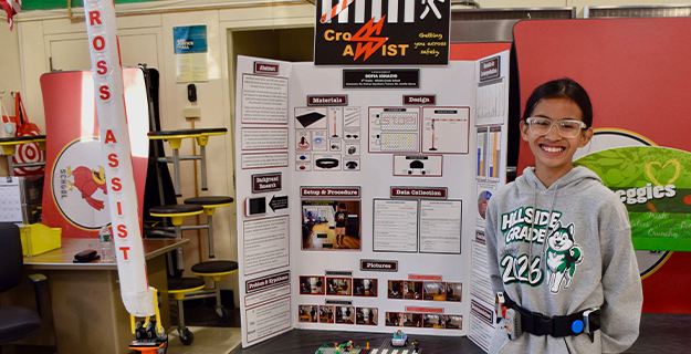 Student smiling proudly in front of science fair project.