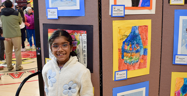 Student standing proudly in front of art exhibit.