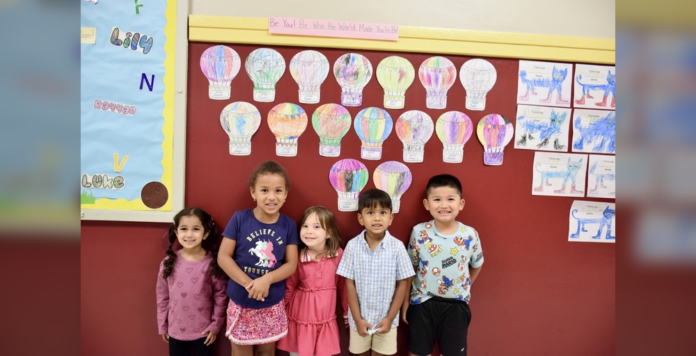 Group of children standing in front of a wall with colorful hot air balloon artwork.