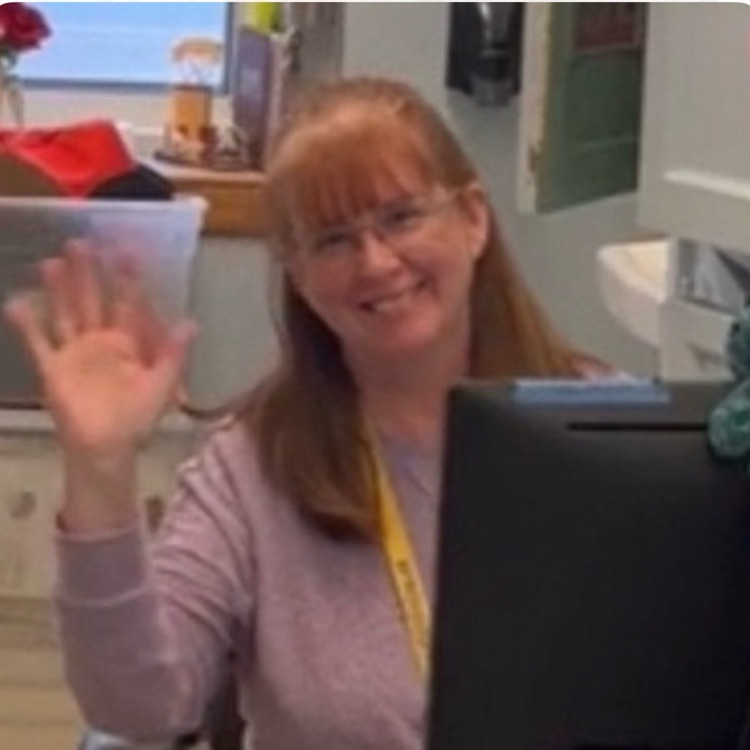 A woman waving by a desk