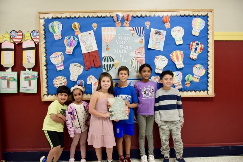 Group of children standing in front of a wall with colorful hot air balloon artwork.