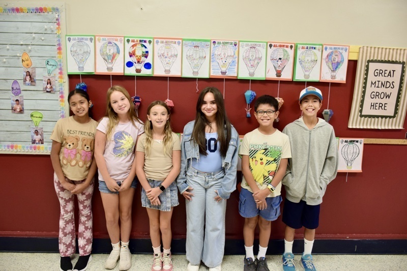 Group of children standing in front of a wall with colorful hot air balloon artwork.