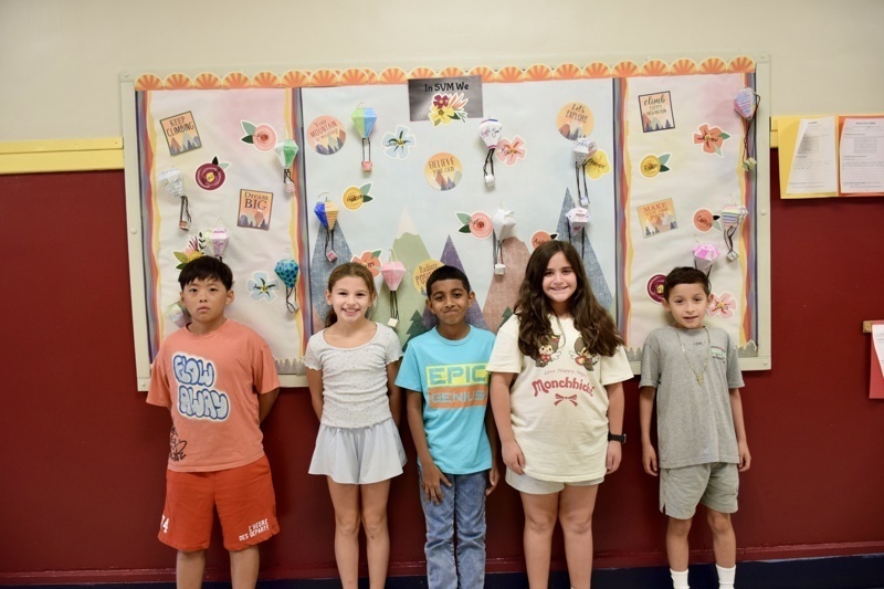 Group of children standing in front of a wall with colorful hot air balloon artwork.